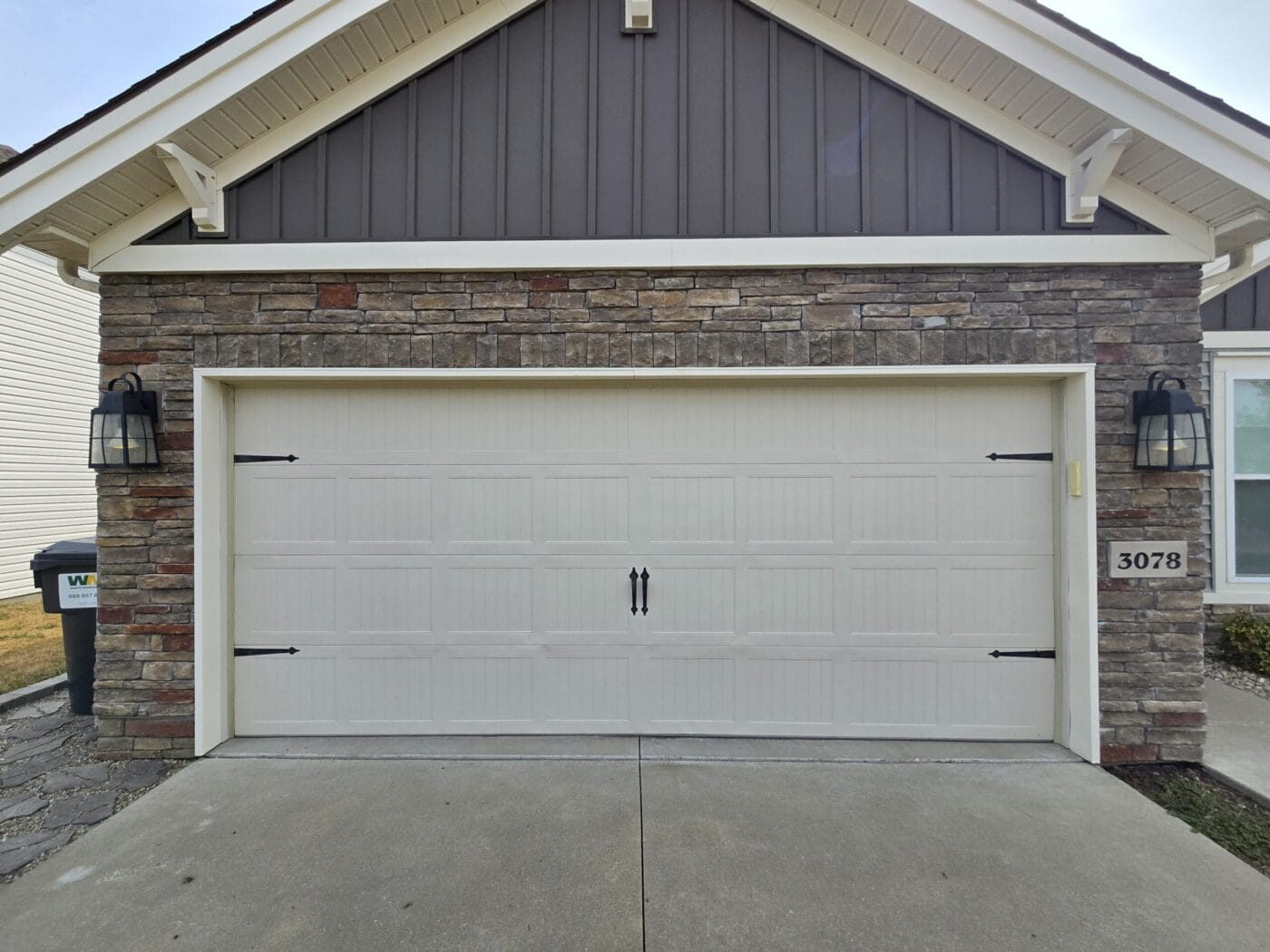 A garage with a stone facade and a double door, featuring two lantern-style lights on either side. House number 3078 is displayed on the right.